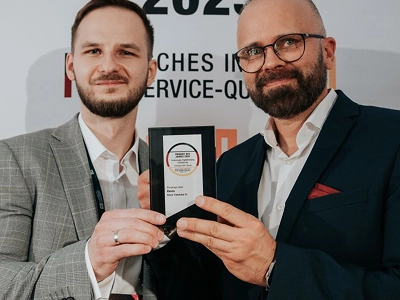 Plataus kadro nuotraukoje užfiksuota apdovanojimų ceremonijos scena, žiūrint iš už sėdinčių žiūrovų nugarų. Kairėje scenos pusėje vyras tamsiai kostiumu ir moteris ilga balta suknele stovi atsukę veidus į minią, rankose laikydami planšetinius kompiuterius. Tamsaus fono scenos centre esančiame dideliame ekrane viršuje šviečia gintarinės spalvos tekstas „WIZJA I INNOVACJE“. Po juo, ekrano centre, matomas didelis, šviečiantis, rombo formos krištolo apdovanojimas, o po juo – tekstas „Maciej Góralski“ ir „Vasco Electronics“. Šiltos, išsklaidytos šviesos apšviečia sceną prieš tamsią, pilną auditoriją.