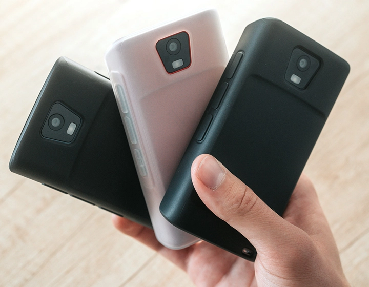 Asmuo, laikantis tris Vasco Translator Q1 įrenginius silikoniniuose dėkluose, demonstruoja tris skirtingas dėklų spalvas: „Solid Black“, „Dark Caramel“ ir „Milky White“.